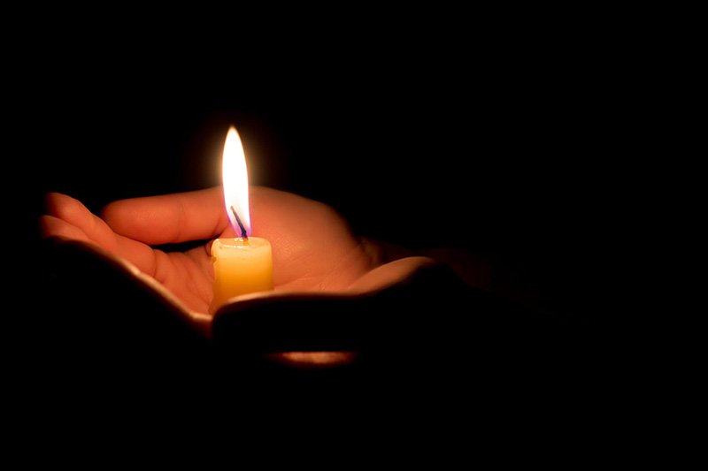 hands holding a burning candle in dark like a heart